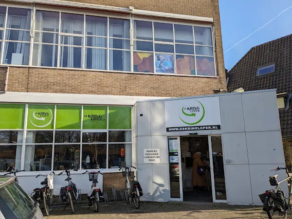 Gevel van kringloopwinkel De Kringloper met groene en witte ramen, winkelnaam zichtbaar, fietsen geparkeerd ervoor