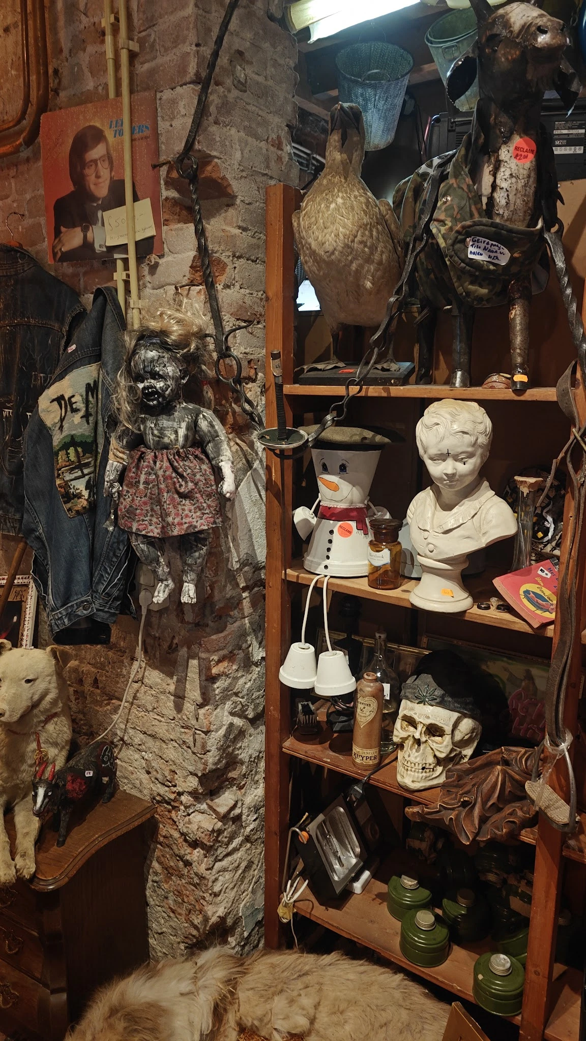 Stellingkast met diverse tweedehandsartikelen: poppen, bustes, servies en decoratieve items