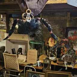 Kringloopwinkelinterieur met uitgestalde spullen, decoraties en een zwarte pluche pop onder een houten kroon.