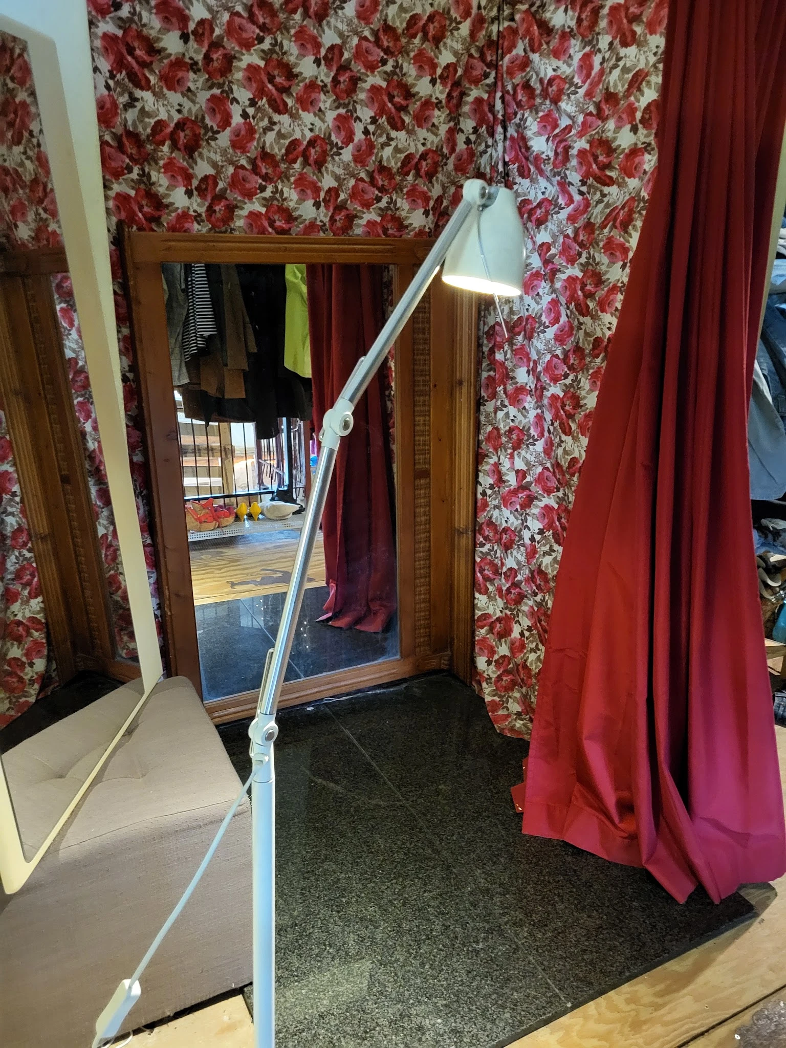 Interieur van kringloopwinkel met rode bloemmotief gordijnen, spiegels en diverse hangend kleding