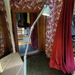 Interieur van kringloopwinkel met rode bloemmotief gordijnen, spiegels en diverse hangend kleding