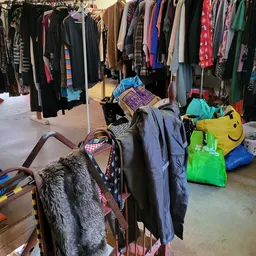 Tweedehands kleding op hangers en in tassen op de winkelvloer