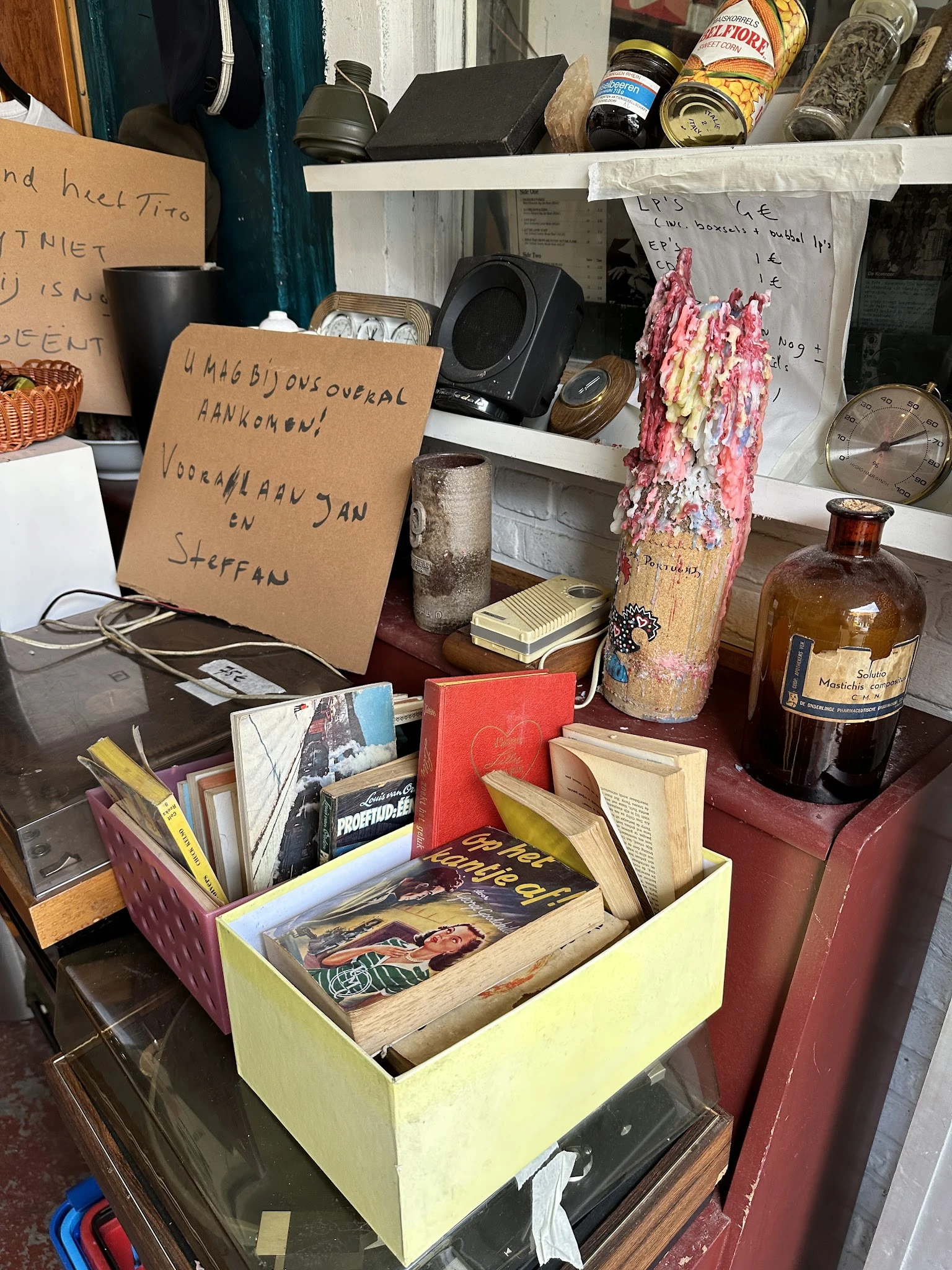 Tweedehands boeken, glazen flessen, decoratieve items en ander huishoudgoed op een shelving unit