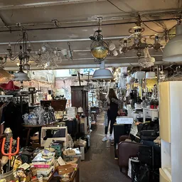 Binnenaanzicht van kringloopwinkel met hanglampen, meubels, kleding en diverse spullen op stellingen en tafels