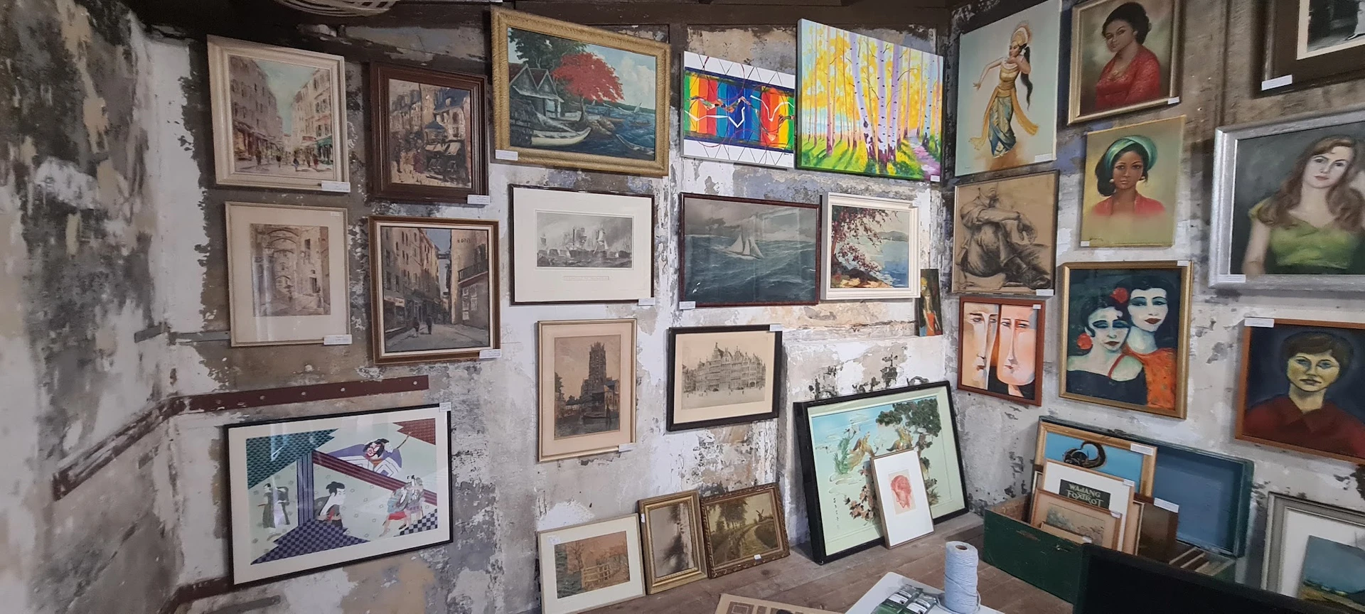 Witte muur volgehangen met diverse ingelijste prenten, schilderijen en kunstwerken in verschillende stijlen en formaten