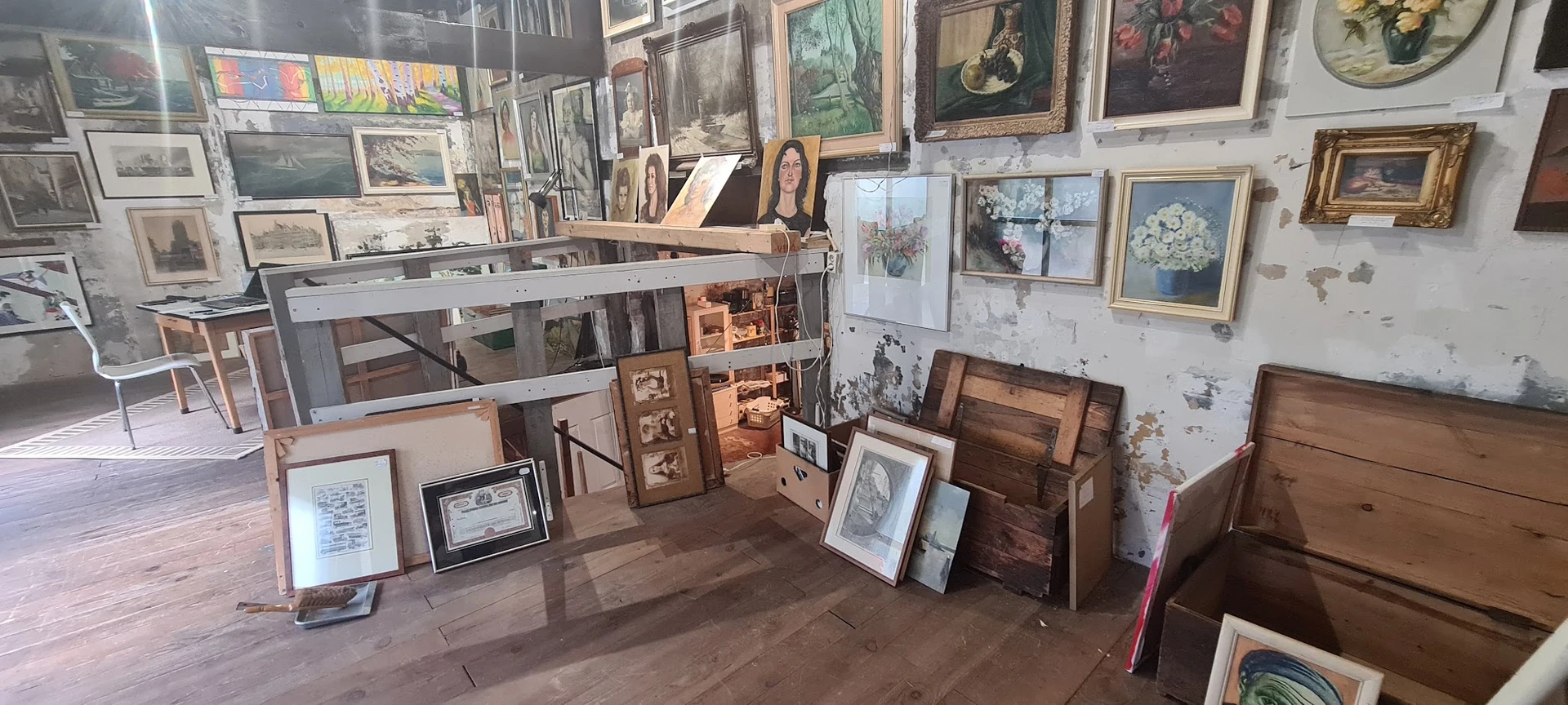 Uitgestalde schilderijen, kunstwerken en houten meubels in een kringloopwinkel