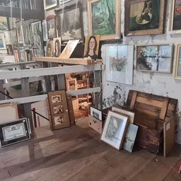 Uitgestalde schilderijen, kunstwerken en houten meubels in een kringloopwinkel