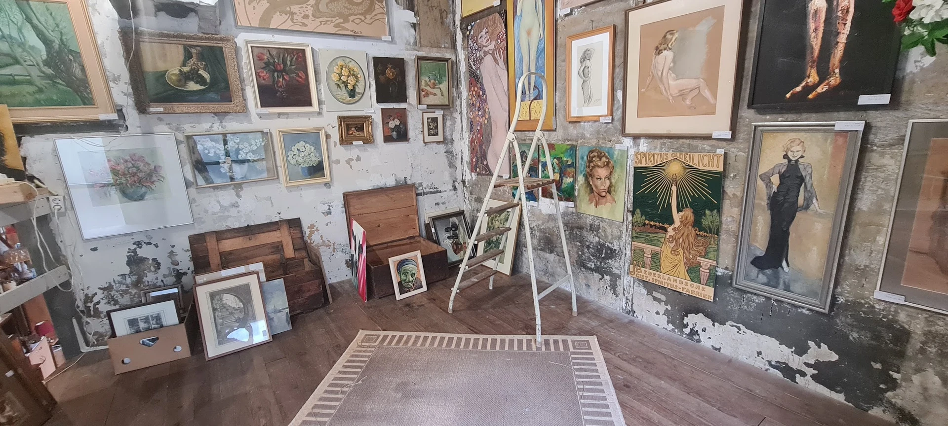 Winkelvloer met kunstwerken aan muren, ladders, houten meubels en kunstzinnige objecten uitgestal