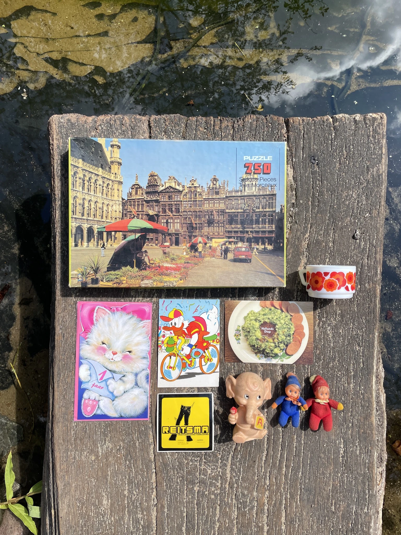Verzameling tweedehands items: puzzel, speelgoed, servies, tape en knuffels op houten ondergrond