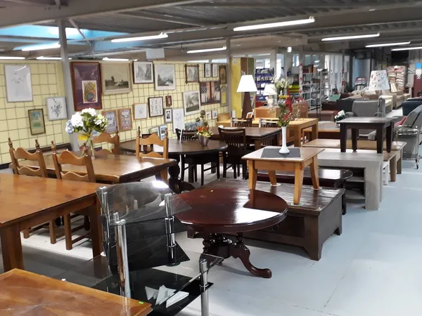 Ruime winkelvloer met houten meubels, tafels, stoelen en kasten, aan de muur veel foto's en decoraties