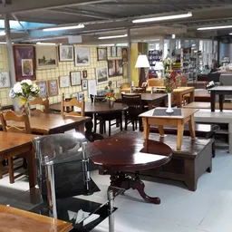 Ruime winkelvloer met houten meubels, tafels, stoelen en kasten, aan de muur veel foto's en decoraties