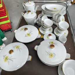 Servies met gele bloemenprint: kommen met deksel, schotels en kopjes in wit porselein met gouden accenten