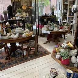 Interieur van kringloopwinkel met houten tafels uitgestald met servies, glazen, kandelaars en decoratieve items