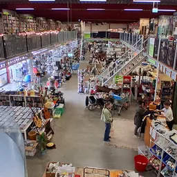 Overzicht van de kringloopwinkelafdeling met stellingen, rekken met diverse goederen en bezoekers die winkelen