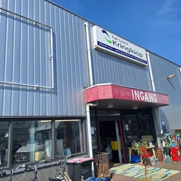 Gevel van kringloopwinkel met rode INGANG-luifel en grijze golfplaten wand