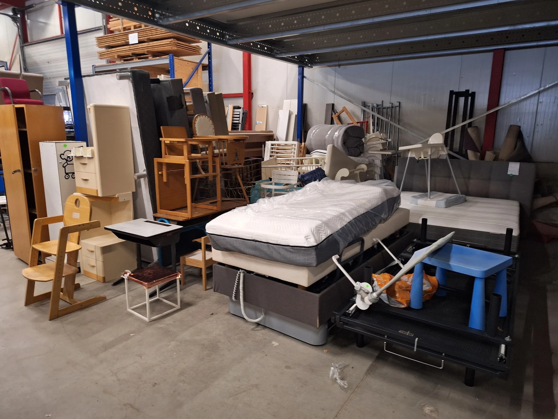 Assortiment tweedehands meubels en huishoudartikelen in kringloopwinkel, waaronder bedden, stoelen, kasten en diversen.