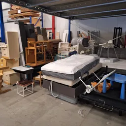 Assortiment tweedehands meubels en huishoudartikelen in kringloopwinkel, waaronder bedden, stoelen, kasten en diversen.