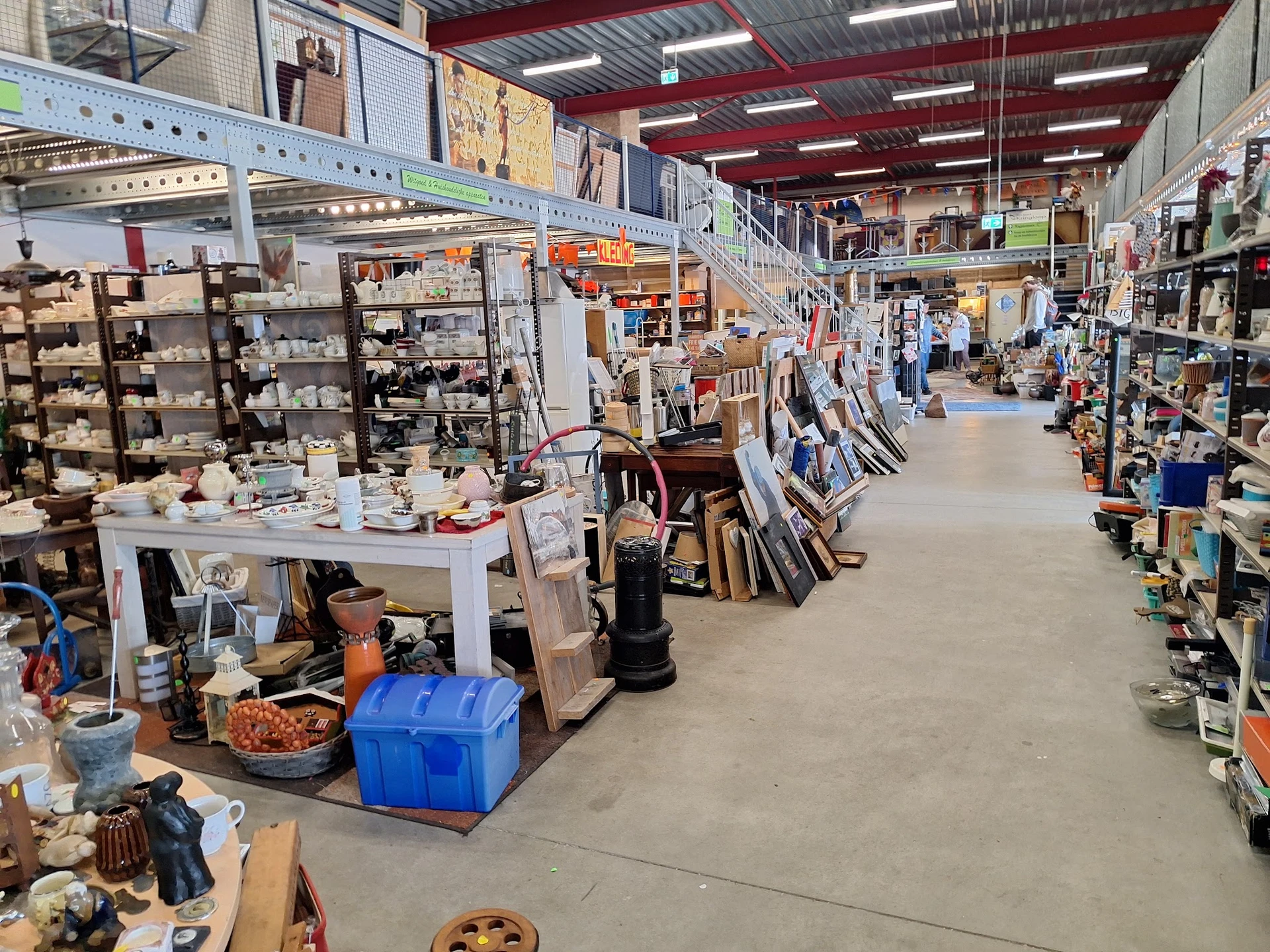 Overzicht van kringloopwinkel met stellingen, tafels met diverse tweedehands artikelen en winkelgang