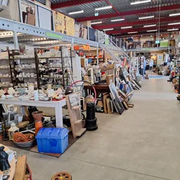 Overzicht van kringloopwinkel met stellingen, tafels met diverse tweedehands artikelen en winkelgang