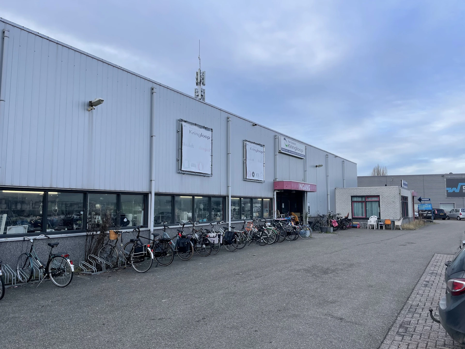 Witte voorgevel van kringloopwinkel met ramen, ingang en fietsen geparkeerd ervoor