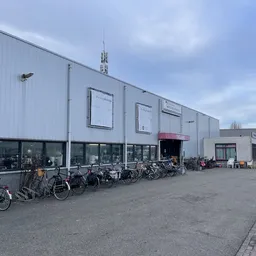 Witte voorgevel van kringloopwinkel met ramen, ingang en fietsen geparkeerd ervoor