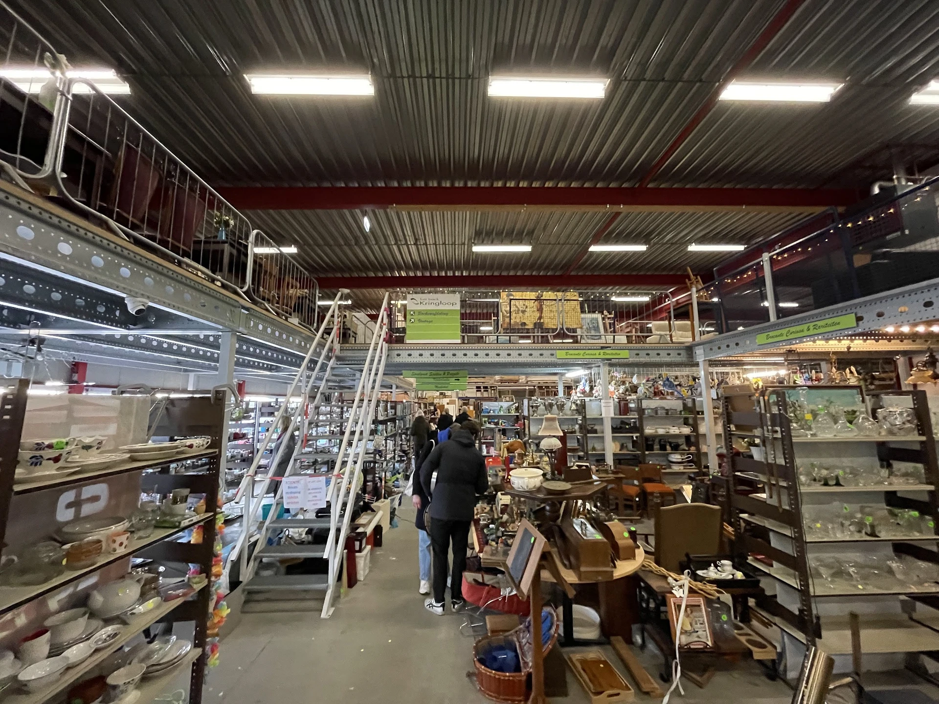 Overzicht van de winkelruimte met stellingen, vitrines en diverse tweedehands spullen langs het gangpad