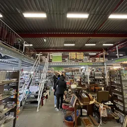 Overzicht van de winkelruimte met stellingen, vitrines en diverse tweedehands spullen langs het gangpad