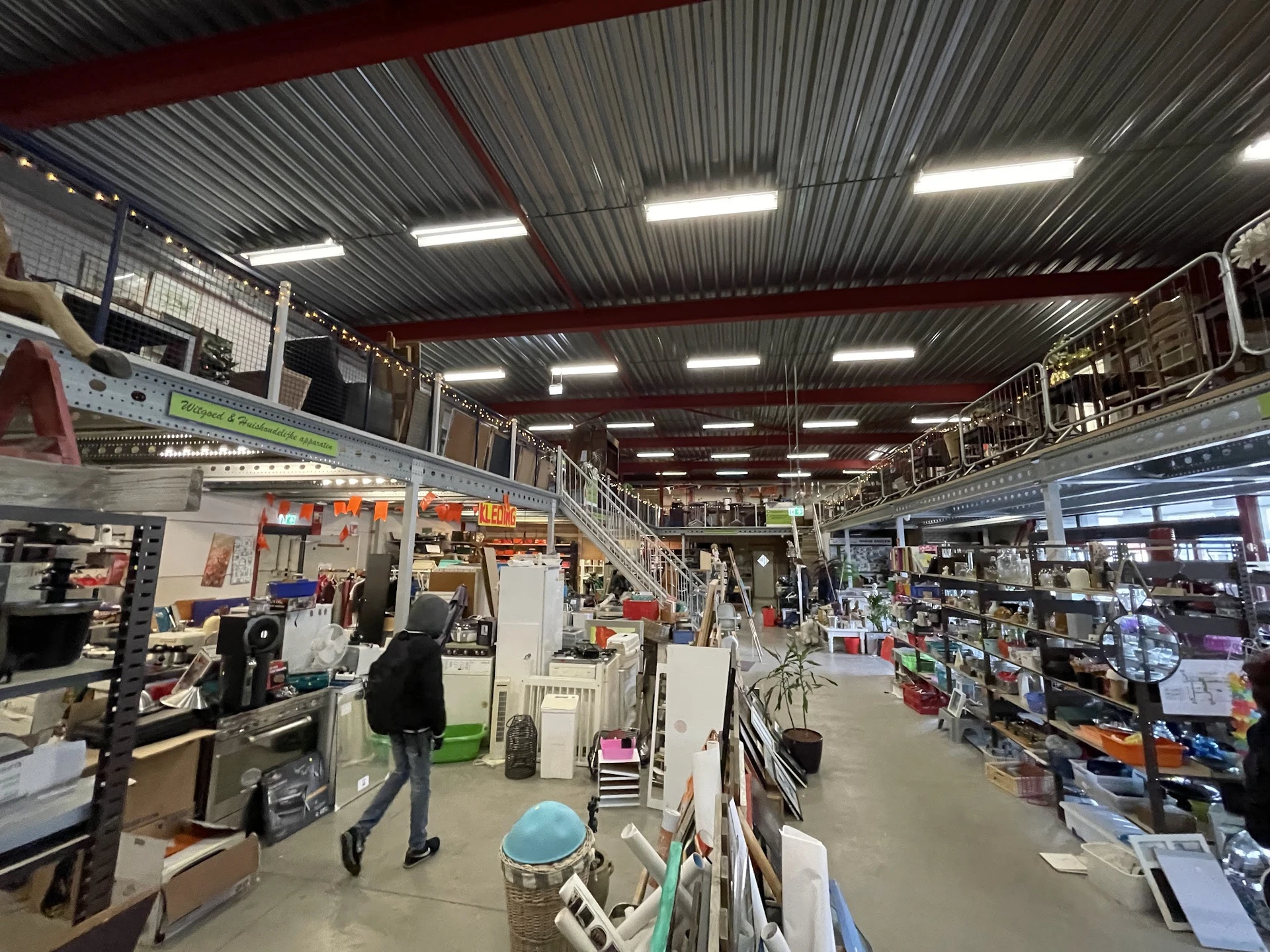 Winkelvloer van kringloopwinkel met stellingen, artikelen en bezoekers in overzicht