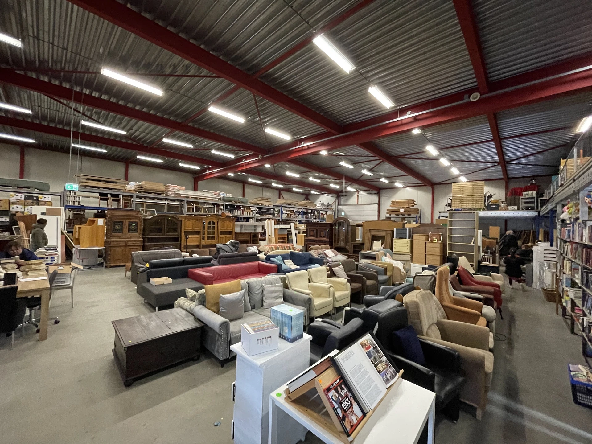 Ruim magazijn met diverse tweedehands meubels zoals banken, fauteuils en kasten, onder LED-verlichting