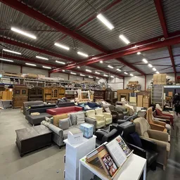 Ruim magazijn met diverse tweedehands meubels zoals banken, fauteuils en kasten, onder LED-verlichting