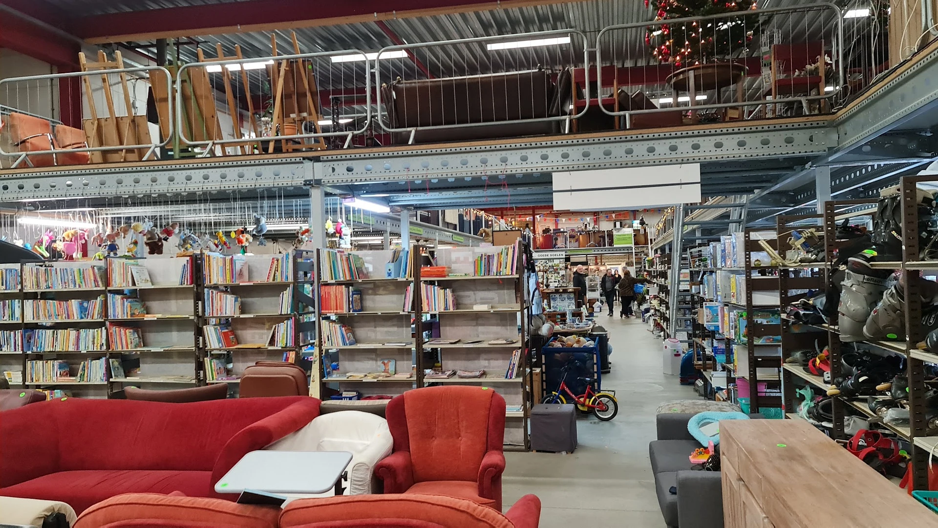 Winkelvloer van kringloopwinkel met boekenrekken, rode zitmeubels en diverse tweedehands artikelen