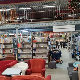 Winkelvloer van kringloopwinkel met boekenrekken, rode zitmeubels en diverse tweedehands artikelen