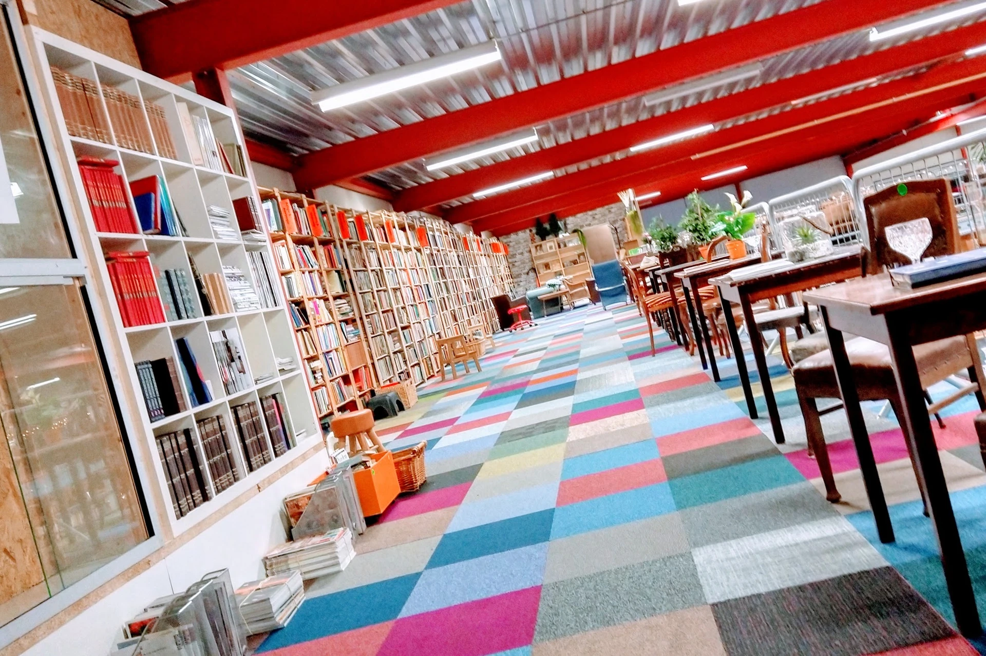 Ruim winkelinterieur met boekenkasten, gekleurde patchwork vloer en rode balkenplafond