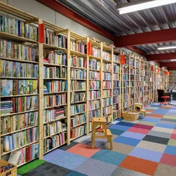 Binnenaanzicht van kringloopwinkel met houten boekenkasten vol tweedehands boeken, gekleurde tegelvloer en rode plafondspante