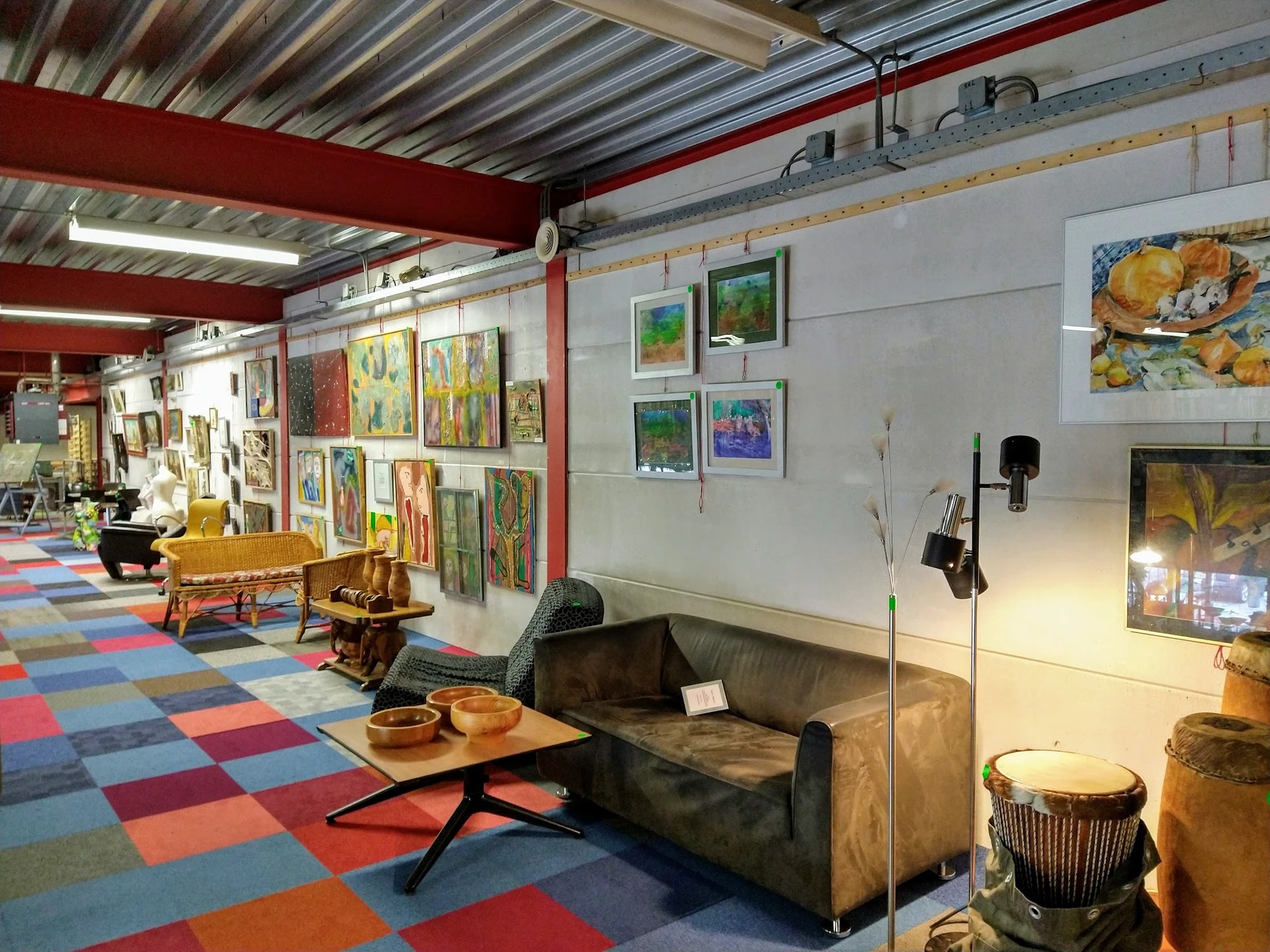Ruim interieur van kringloopwinkel met kleurrijke vloer, kunstwerken aan wanden, meubels en huisraad