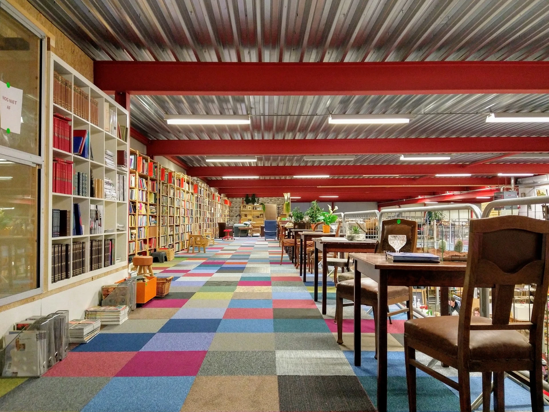 Ruim winkelinterieur met boekenkasten, kleurrijk geblokt tapijt en houten meubels onder rode dakbalken