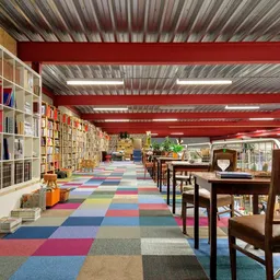 Ruim winkelinterieur met boekenkasten, kleurrijk geblokt tapijt en houten meubels onder rode dakbalken
