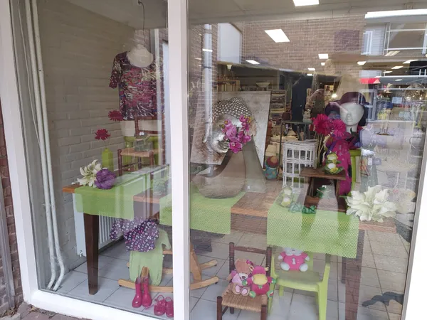 Winkelraam met groene en paarse decoratie, jurken, bloemen en huisraad op display