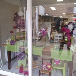 Winkelraam met groene en paarse decoratie, jurken, bloemen en huisraad op display