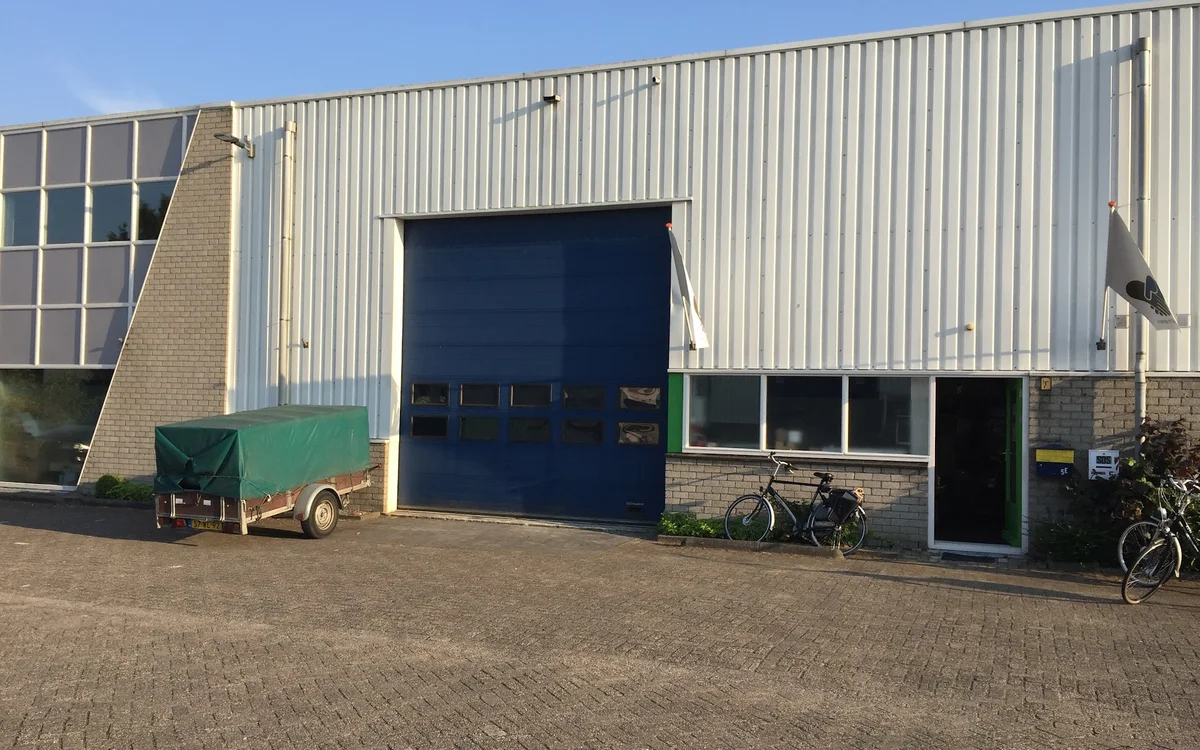 Voorgevel van kringloopwinkel met blauwe rolluik, groene ingang en bakstenen zijvleugel