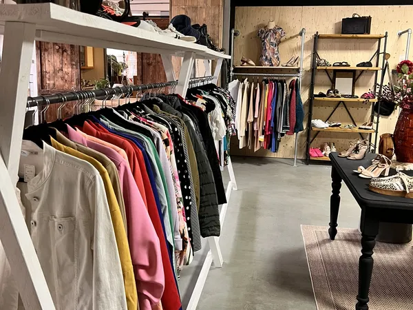 Kringloopwinkel met kledingrekken, houten stellingen en een zwarte tafel met accessoires