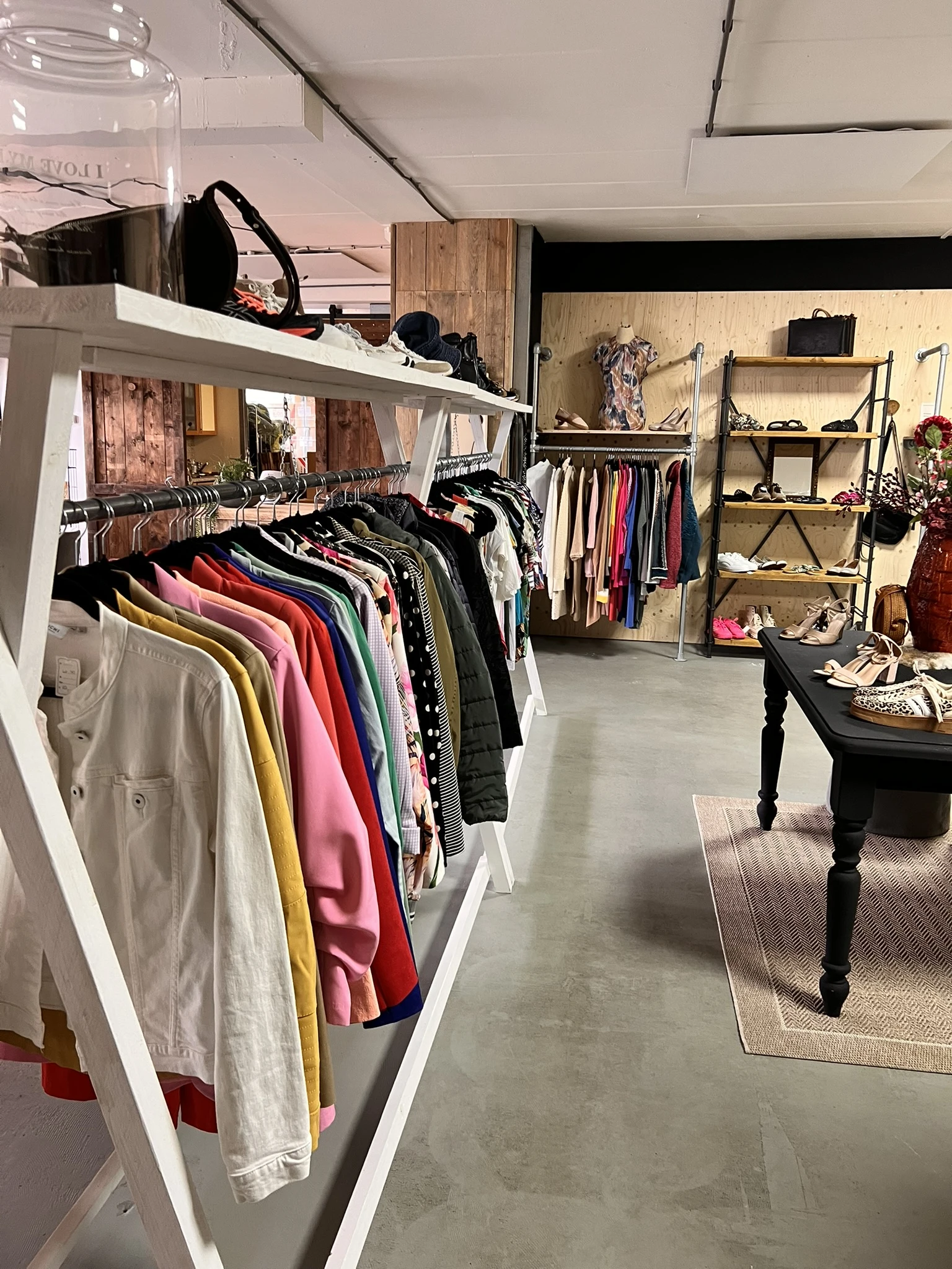 Kringloopwinkel met kledingrekken, houten stellingen en een zwarte tafel met accessoires
