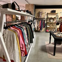 Kringloopwinkel met kledingrekken, houten stellingen en een zwarte tafel met accessoires