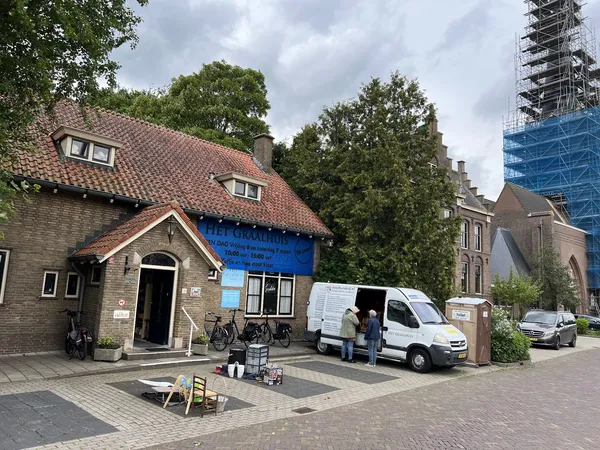 Voorgevel van een kringloopwinkel met rode dakpannen, blauwe deur en witte bestelbus geparkeerd voor de ingang