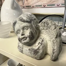 Stenen decoratief beeldje van een cherubijn of engel op een winkelplank