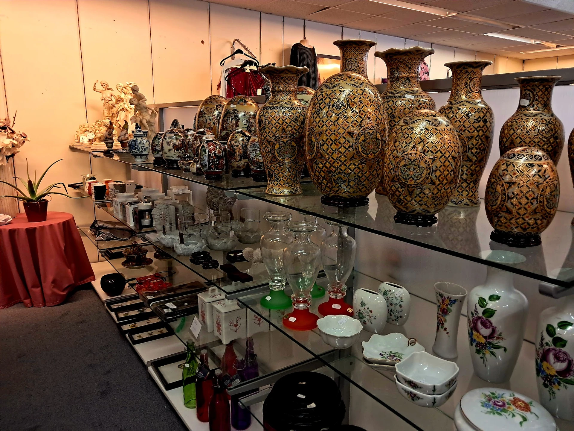Uitgestalde collectie decoratieve vazen en serviesgoed in vitrinekast met gouden en bloemenmotieven