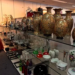 Uitgestalde collectie decoratieve vazen en serviesgoed in vitrinekast met gouden en bloemenmotieven
