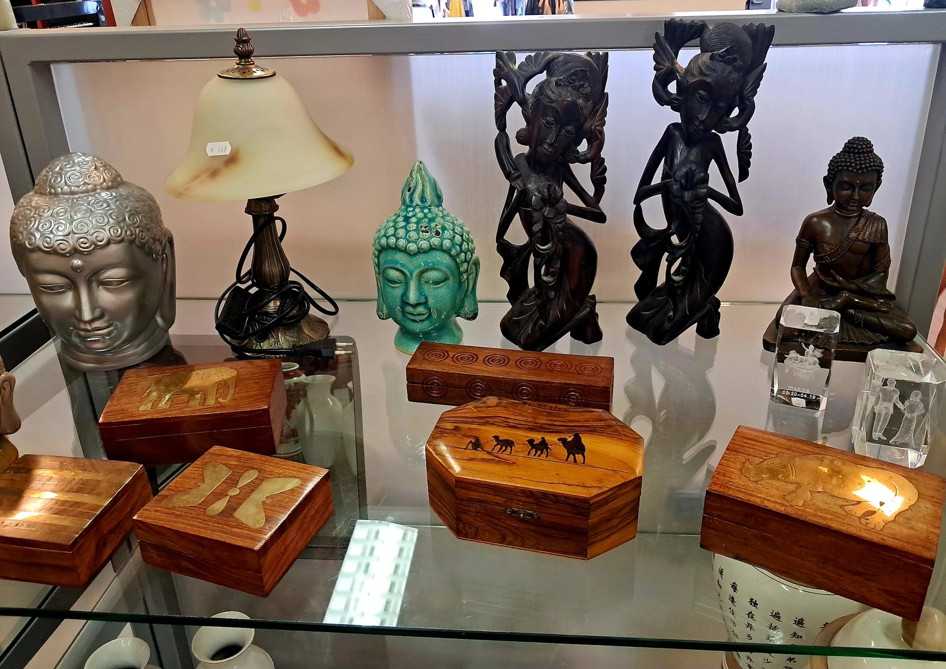 Glazen vitrine met decoratieve objecten: Boeddhahoofden, houten kistjes, beeldhouwwerken en bronzen figuurtjes.