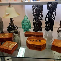 Glazen vitrine met decoratieve objecten: Boeddhahoofden, houten kistjes, beeldhouwwerken en bronzen figuurtjes.