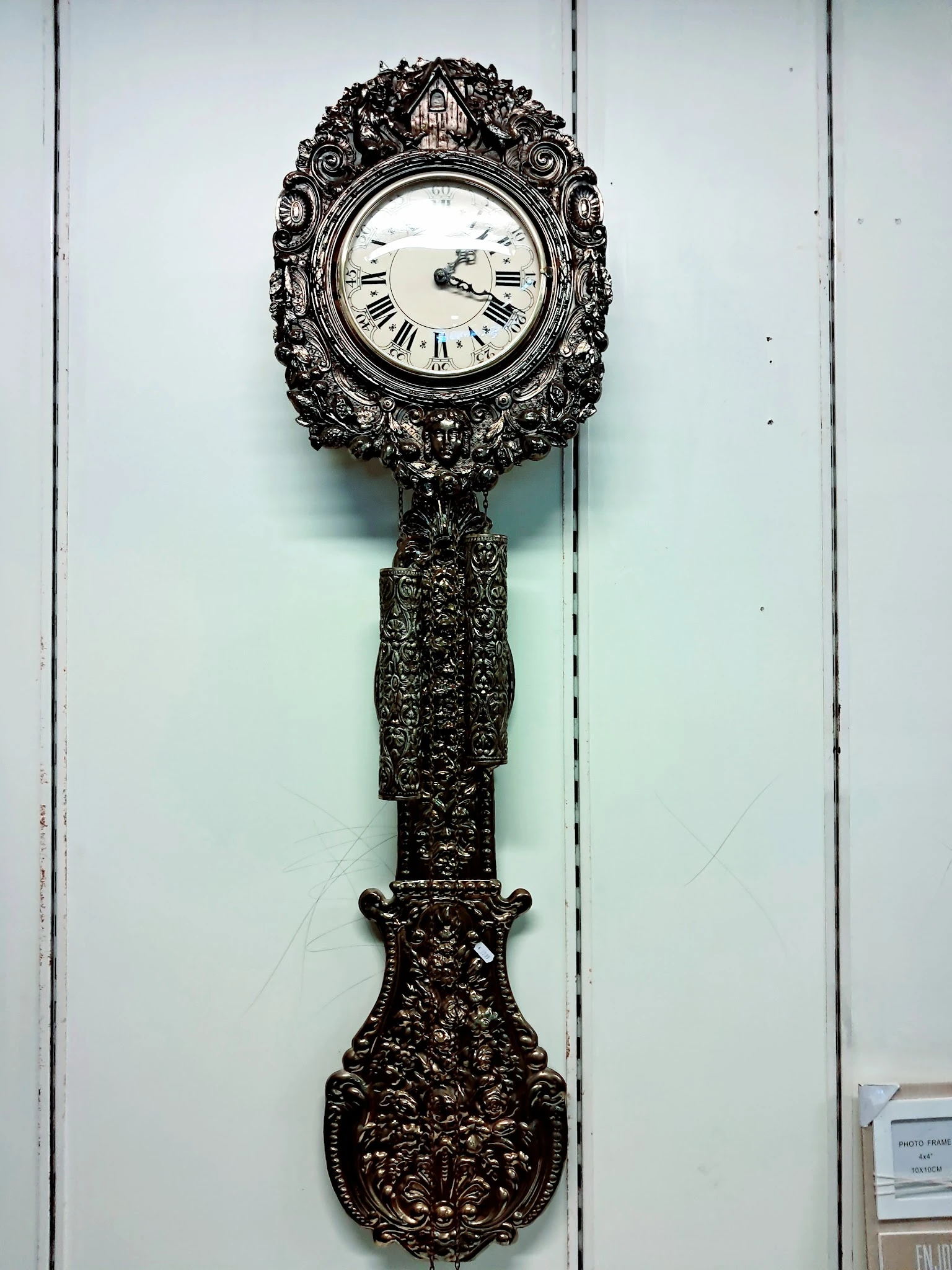 Zwart ornamentaal wandklok met uitgebreide decoratieve stijl en Romeinse cijfers op de wijzerplaat